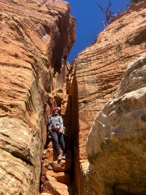 A climber in a helmet navigates a narrow rock crevice under a clear blue sky.