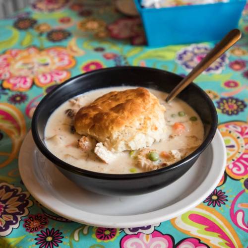 A bowl of creamy chicken and biscuit soup on a colorful floral tablecloth.