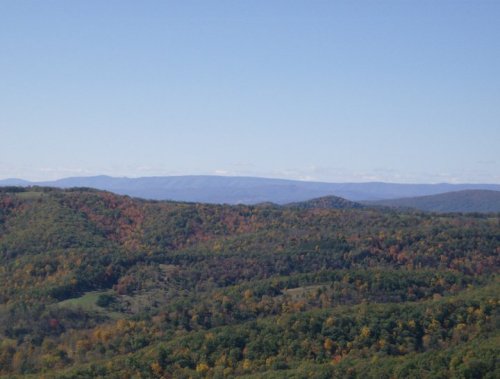 A scenic view of rolling hills and valleys, showcasing vibrant autumn foliage under a clear blue sky.