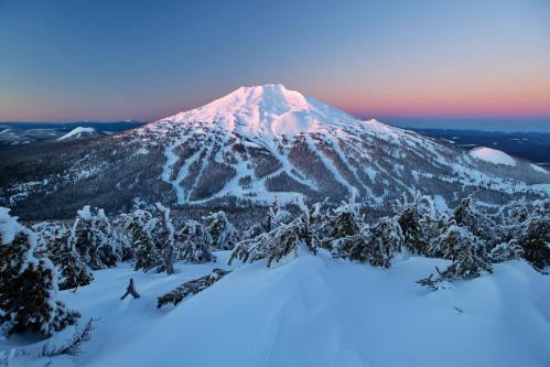 Snow-covered mountain at dusk, with a gradient sky and trees in the foreground, creating a serene winter landscape.