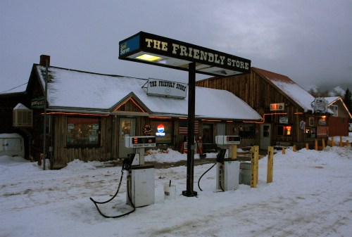 A snowy scene featuring "The Friendly Store" with gas pumps and rustic buildings in a winter landscape.
