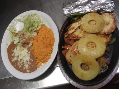 A plate of grilled chicken with pineapple, served with rice, beans, lettuce, and pico de gallo on the side.