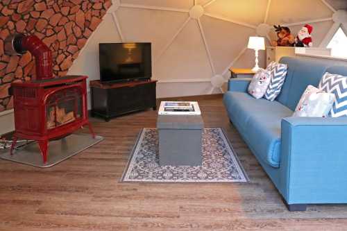 Cozy living space with a blue sofa, coffee table, TV, and a red stove, featuring a patterned rug and warm lighting.