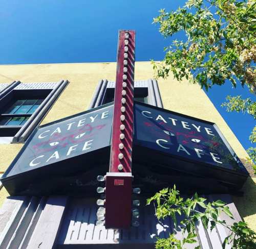 Sign for Cat Eye Cafe against a clear blue sky, featuring bright lights and a bold design.
