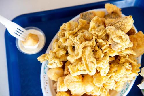 A plate of crispy fried seafood, including calamari and fish, served with a small cup of dipping sauce.