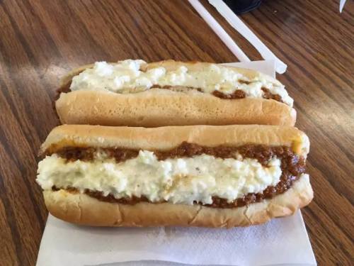Two hot dog buns filled with a creamy white topping and a brown, chunky filling, placed on a wooden table.