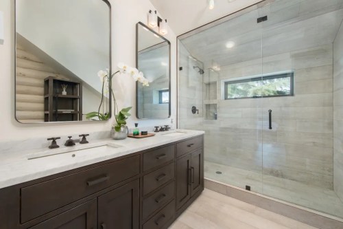 Modern bathroom featuring a double sink vanity, large glass shower, and natural light from a window.