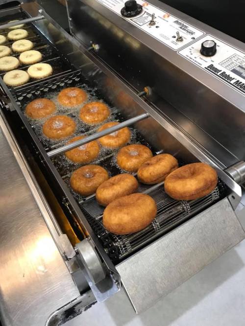 Freshly fried donuts in a commercial fryer, with some donuts floating on top and others submerged in hot oil.