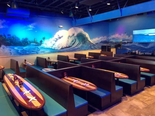 Interior of a restaurant featuring blue wave mural, wooden tables, and cozy booths with teal seating.