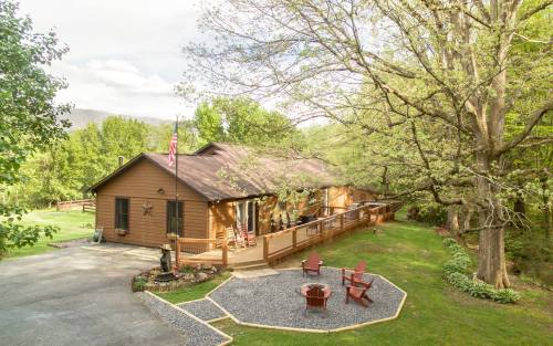 A cozy brown cabin surrounded by greenery, featuring a porch, fire pit, and a flag in a serene outdoor setting.