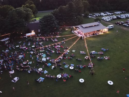 Aerial view of a lively outdoor gathering with people on blankets, string lights, and a building in the background.