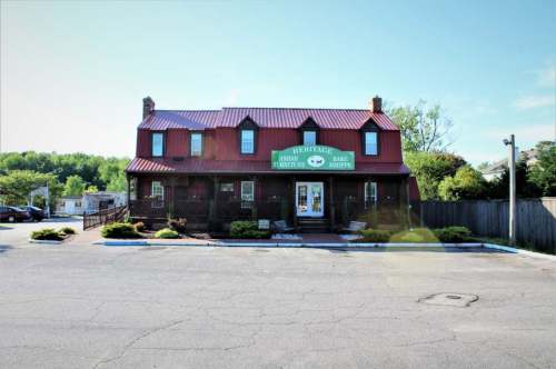 A two-story building with a red metal roof and green signage, surrounded by greenery and a parking area.
