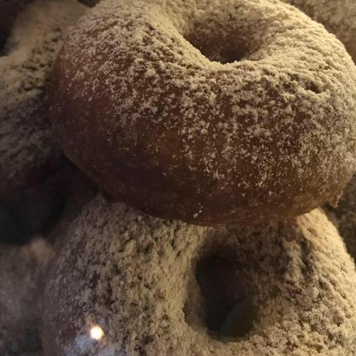 A close-up of a powdered sugar-coated donut resting among other donuts.