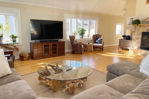 Bright living room with a large TV, wooden furniture, a glass coffee table, and cozy seating by a fireplace.