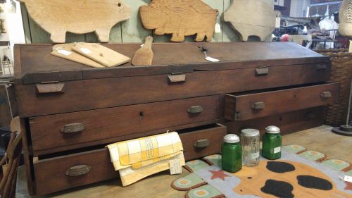 A vintage wooden chest with multiple drawers, surrounded by rustic decor items and jars on a table.