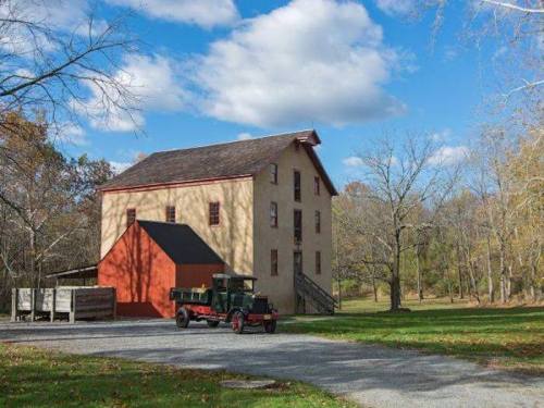 Historic building with a red roof and an old truck parked in front, surrounded by trees and a blue sky.