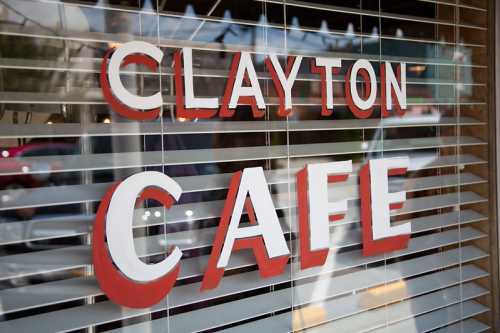 Sign reading "Clayton Cafe" on a window with blinds partially closed.