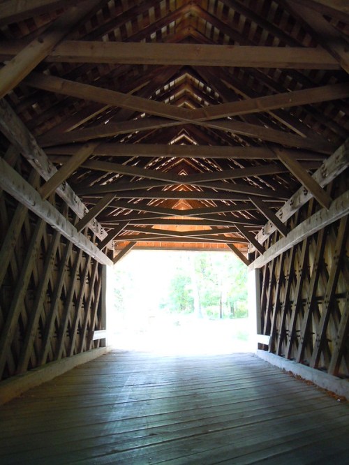 View from inside a wooden covered bridge, showcasing a rustic ceiling and light streaming in from the entrance.