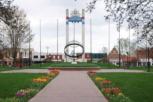 A park with a circular sculpture, colorful tulips, and a sign reading "Tulip Time" in a small town setting.