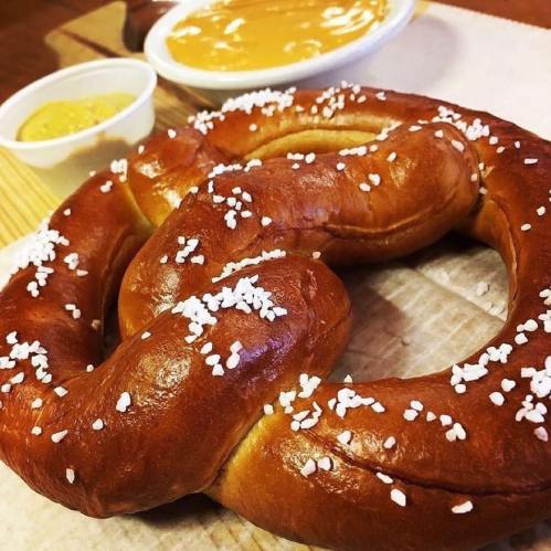 A large, soft pretzel sprinkled with coarse salt, accompanied by mustard and cheese dip in small bowls.