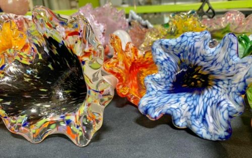 Colorful glass art pieces in floral shapes, featuring vibrant swirls and patterns, displayed on a dark surface.