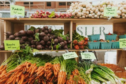 A wooden display of fresh vegetables, including radishes, beets, carrots, and salad turnips, with price tags.