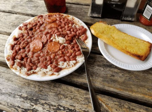 A plate of rice and red beans with sauce, accompanied by a slice of cornbread on a paper plate.