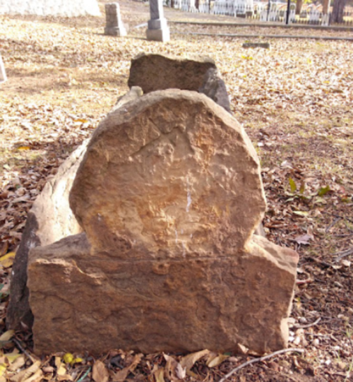 Weathered gravestones in a cemetery, surrounded by fallen leaves and a peaceful, natural setting.