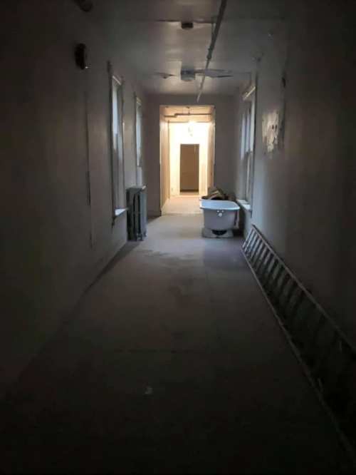 A dimly lit hallway with a ladder, a bathtub, and a light at the far end.