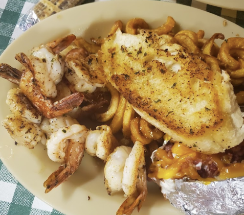 A plate of curly fries topped with cheese, grilled fish, and seasoned shrimp.