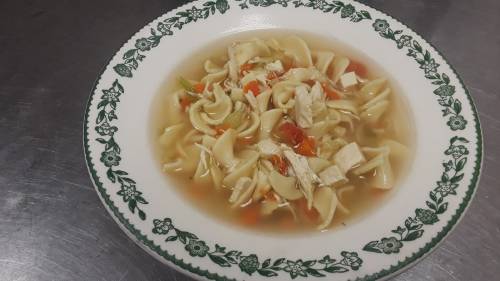 A bowl of chicken noodle soup with noodles, shredded chicken, and vegetables in a clear broth, garnished with herbs.
