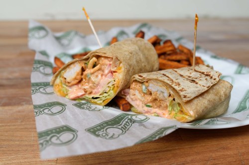 A close-up of a chicken wrap filled with sauce and vegetables, served with sweet potato fries on the side.