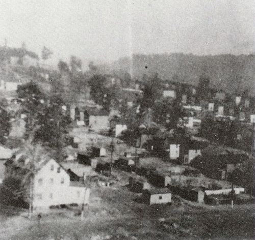 A blurred black-and-white image of a small town with scattered houses and trees in the background.