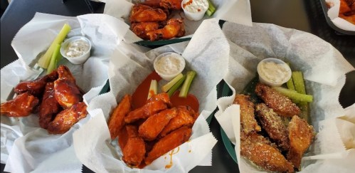 Four baskets of chicken wings with celery sticks and dipping sauces on a table.