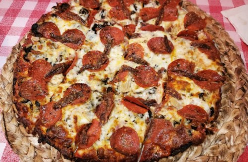 A freshly baked pizza topped with pepperoni and cheese, served on a woven platter with a checkered tablecloth.