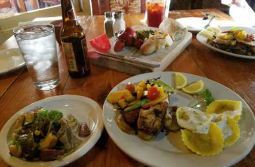 A table set with two plates of food, a glass of water, a beer, and a variety of side dishes and bread.