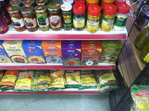 A shelf displaying various jars and boxes of spices, grains, and mixes in a grocery store.