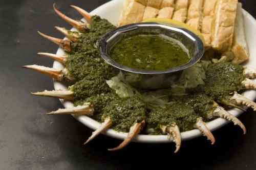 A plate of crab claws arranged around a bowl of green sauce, with pieces of bread on the side.
