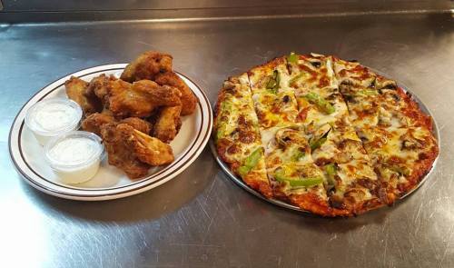 A plate of crispy chicken wings with two dipping sauces next to a large pizza topped with vegetables and cheese.