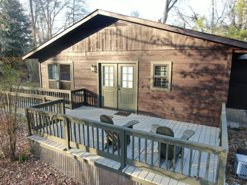 A wooden cabin with a deck and chairs, surrounded by trees in a natural setting.