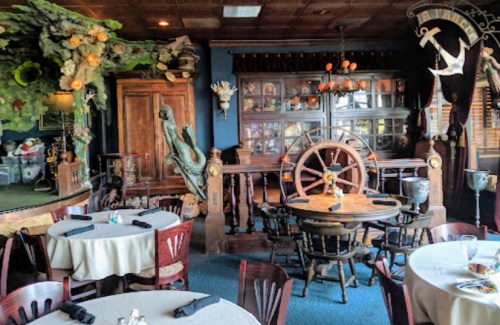 Cozy restaurant interior with wooden decor, nautical elements, and round tables set for dining.