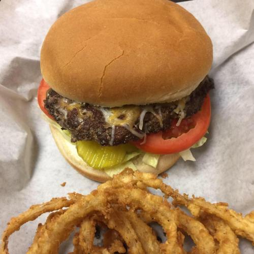 A juicy burger with lettuce, tomato, pickles, and cheese, served with crispy onion rings on the side.