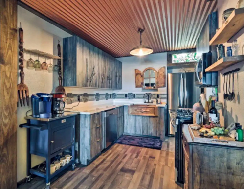 A rustic kitchen with wooden cabinets, a stainless steel fridge, and a countertop filled with fresh vegetables.