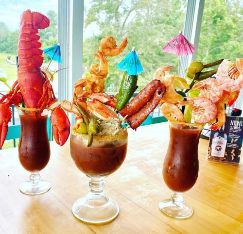 Three colorful seafood cocktails with shrimp, lobster, and garnishes, served in tall glasses on a wooden table.