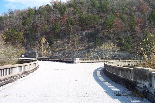 A winding road leads through a natural landscape with trees and rocky hills in the background.