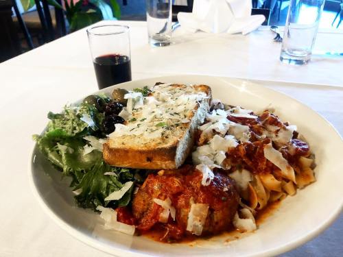 A plate of pasta with meatballs, garlic bread, salad, and a glass of red wine on a white tablecloth.