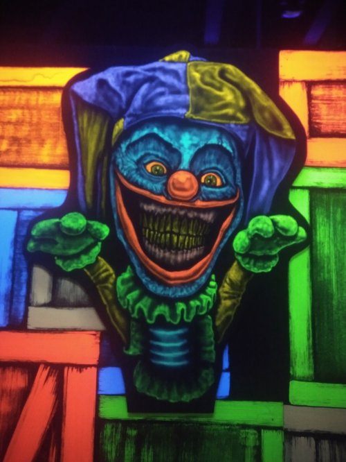 A vibrant, glowing clown with a sinister grin, framed by colorful, abstract shapes in a dark setting.
