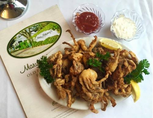 A plate of fried soft-shell crabs garnished with parsley, accompanied by lemon wedges and dipping sauces.