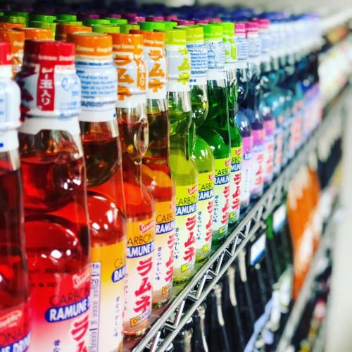 A colorful display of various flavored ramune soda bottles on a store shelf.