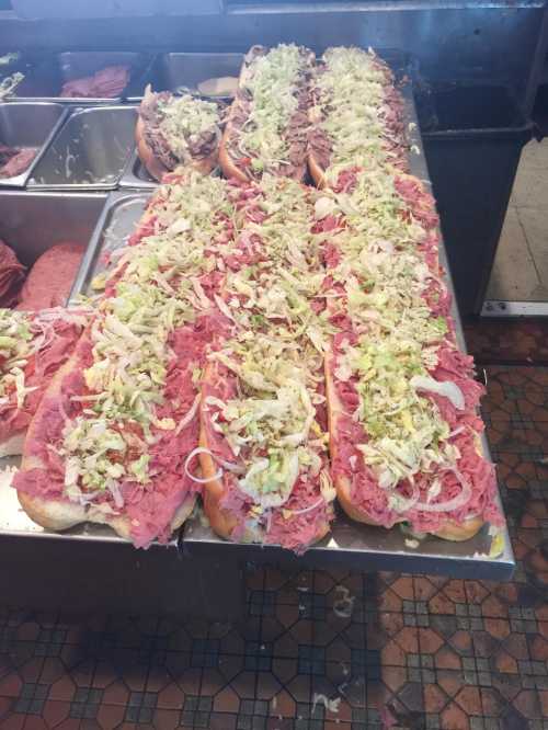 A row of large sandwiches filled with layers of meat and topped with shredded lettuce on a countertop.